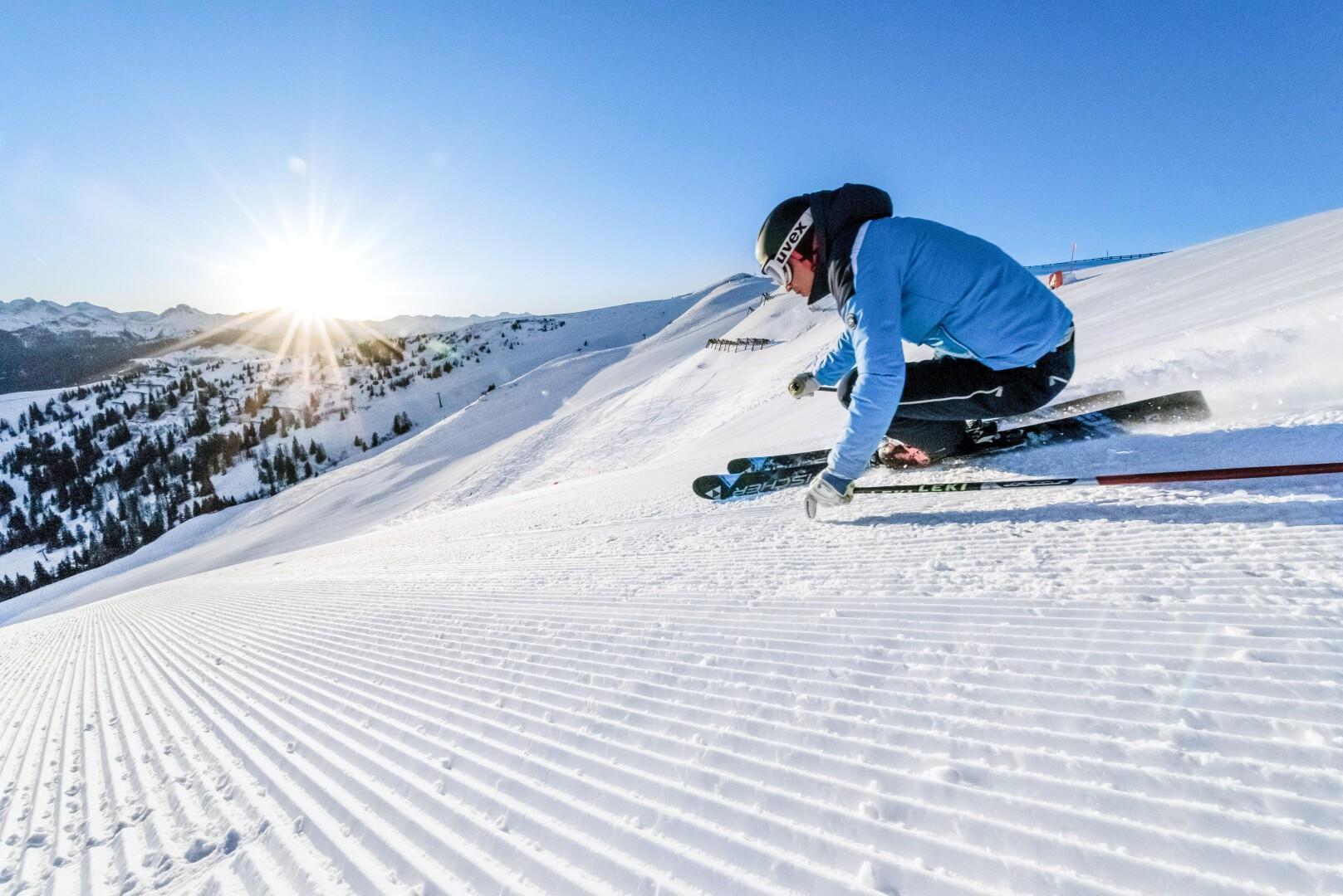 Skier de carvend naar beneden knalt op strak geprepareerde piste met zon op de achtergrond in Gastein
